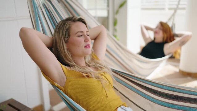 Two women relaxed lying on hammock at home terrace