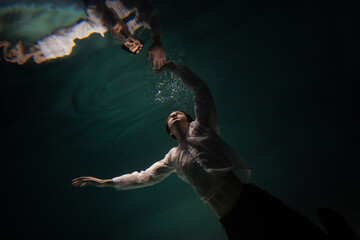 underwater shooting with contrasting light, a guy is swimming underwater, pulling his hand to his...