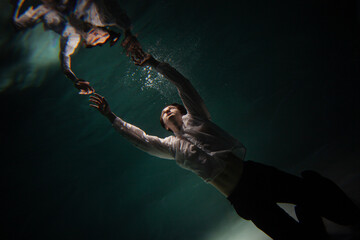 Photo underwater, a guy in a white shirt floundering underwater and reaching for the surface of the...