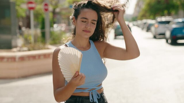 Young beautiful hispanic woman using handfan suffering for hot at street