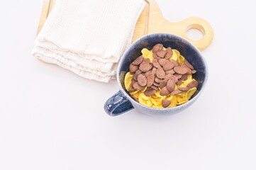 ciotola artigianale con fiocchi di cereali, canovaccio bianco e tagliere in legno su tavolo bianco