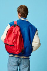 a guy in a fashionable jacket stands with his back to the camera showing his red backpack for study