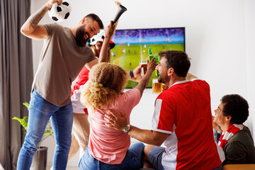 Friends cheering, making a toast and drinking beer while watching football on TV