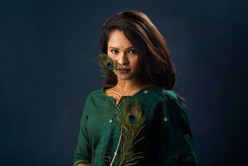 Beautiful Young Girl posing with peacock feathers on grey background.