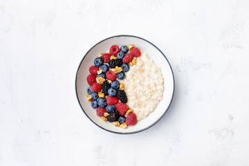Bowl of oatmeal porridge with blueberry and raspberry on white table top view. Yummy and diet breakfast.