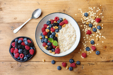 Bowl of oatmeal porridge with various berry on wooden table top view. Healthy and diet breakfast.