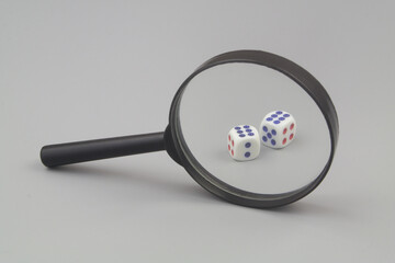 Dices under magnifying glass on gray background. Gambling review concept.