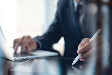 Businessman using stylus pen signing e-document on digital tablet with laptop computer on table at...