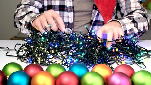 Male hands trying to prepare xmas unravel the tangled glowing lights of Decorative Christmas garland at home.