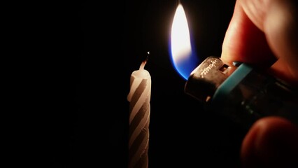 a lighter lights a small striped candle in the dark.  - Powered by Adobe