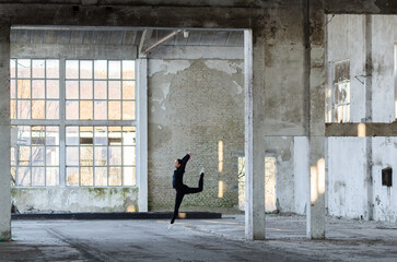 Fototapeta na wymiar Ballerina jumping and dancing in an abandoned building on a sunny day