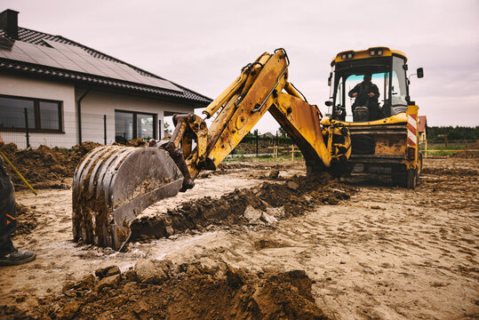 Excavator working at house construction site - digging foundations for modern house. Beginning of house building. Earth moving and foundation preparation.
