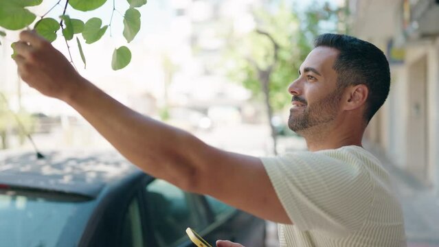 Young hispanic man smiling confident making photo to tree sheet at street