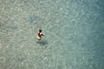 Aerial view to azure sea and woman in bikini go to swim in transparent water. Girl swimmer, beach...