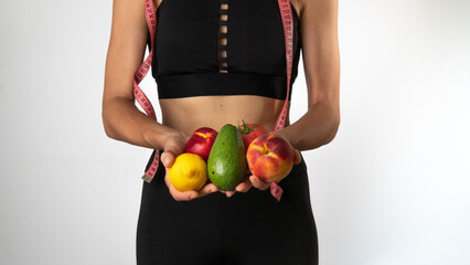 A woman in sportswear holds vegetables and fruits in her hands, a measuring tape - proper nutrition and sports