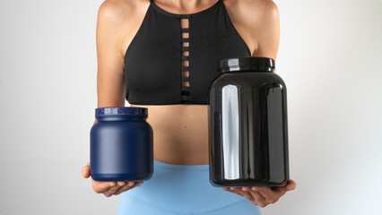 Athletic slender woman holding cans of protein and sports supplements for an effective workout in the gym