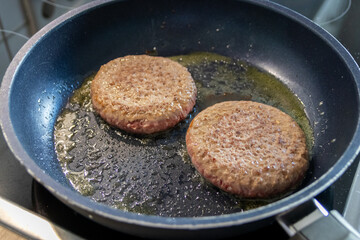 Two burger patties burger meat sizzling in hot pan with fat and oil as delicious selfmade hamburger bbq meatballs as unhealthy fast food lunch with lots of calories and cholesterol in frying pan