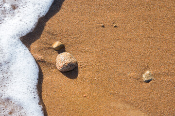Wave on sandy beach, white foam an sand.
