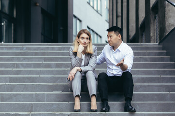 Business colleagues man and woman sitting together on stairs, Asian man comforting and comforting...