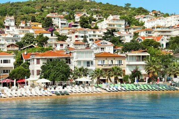 Snow-white cottages with tiled roofs on a hillside near the sea, sun loungers on the beach