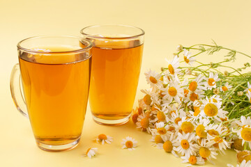 Infusion (decoction, tea) of chamomile medicinal (pharmacy) in two glass mugs on a yellow background close-up.