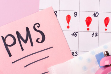 Calendar of women's menstruation, the inscription of PMS on the sheets for notes on a pink background close-up. The period (time) of critical days. Women's health.