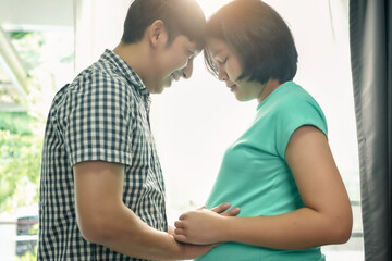 Asian husband stroking his pregnant wife's belly happily