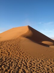 Fototapeta na wymiar Huge big orange yellow sand dune with walker expedition group footprints path up to the top in the desert in Namibia Africa with blue sky background success achievement concept