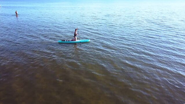 A young woman floats on a turquoise SUP board in a pond. Aero shooting