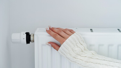 Close-up of a woman in white sweater warms her hands over the battery on background of white...