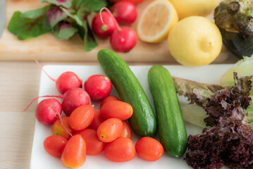 Top view cherry tomatoes They are placed in a tray with radishes, cucumbers, red oak lettuce and other fruits and vegetables. As a raw material for making salads on the kitchen table.