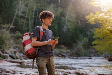 Young man traveler with backpack looking for route on smartphone at river in mountains.