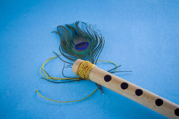 Bamboo flute decorated with peacock feather symbolic to hindu god lord krishna during celebration of janmashtami festival. photo taken in blue background with copy space.