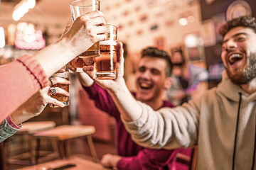 Happy group of young friends at pub cafe raising beer glasses for a celebratory toast - filtered...