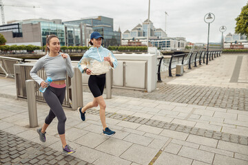 Two athletic women in sportswear are running around the city. Reaching the goal