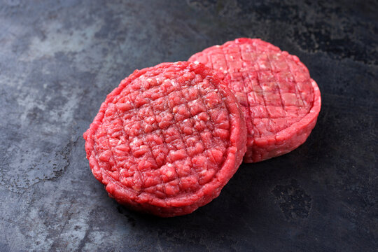 Raw barbecue beef Hamburger patty offered as close-up on rustic black background with copy space