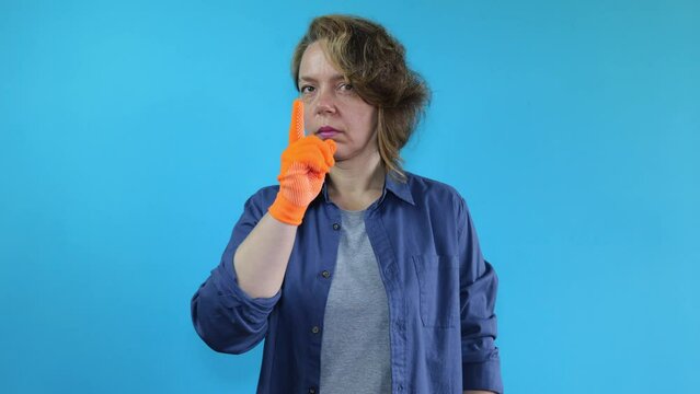 Forty year old woman in a shirt covers her mouth with masking tape on an isolated blue background. Woman in orange gloves