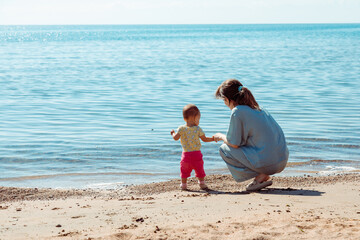 Mother with baby playing with stones by the water on a beach