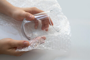 Woman hands packaging a glass for water with white transparent bubble wrap on a white background....