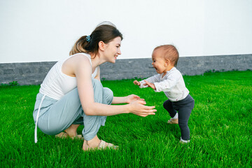 Baby learning to take first steps rushing to mother's hands outside on lawn