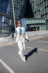 Naklejka premium Beautiful woman in trendy outfits crosses road against backdrop of city buildings