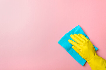 Employee hand in yellow rubber protective glove hold blue rag wiping pink wall background. House cleaning service, general or regular cleanup concept. Empty place for text or design
