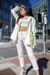 Fototapeta premium Attractive woman in trendy outfit standing on skyscrapers cityscape background
