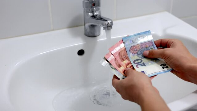 Euro Banknotes On The Background Of Running Water In The Tap In The Bathroom. Cost Calculation According To The Tariff Concept. Household Efficiency And Cost Idea. The Concept Of Saving Water