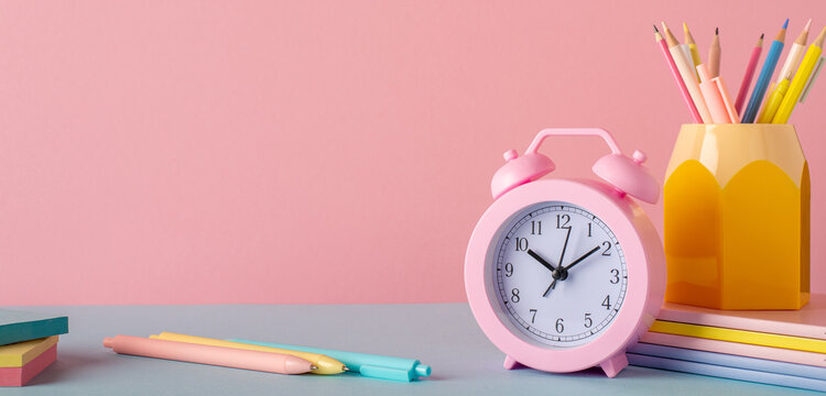 Back to school concept. Photo of school accessories on blue table pencil holder alarm clock stack of notebooks and pens on pastel pink wall background - Powered by Adobe