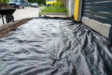 The plowed garden in front of the fence in the house, covered with black agrofiber, visible black...