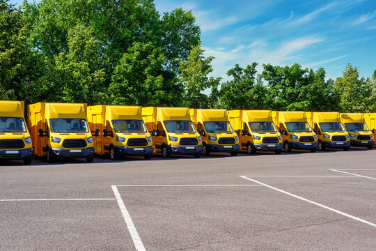 A Fleet Of Yellow Electric Delivery Vans Parking In Front Of Green Trees.