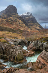 Obraz premium Gorgeous landscape image of vibrant River Coe flowing beneath snowcapped mountains in Scottish Highlands