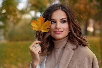 Happy autumn woman with fall yellow maple leaf portrait. Beautiful model with curly hairstyle .
