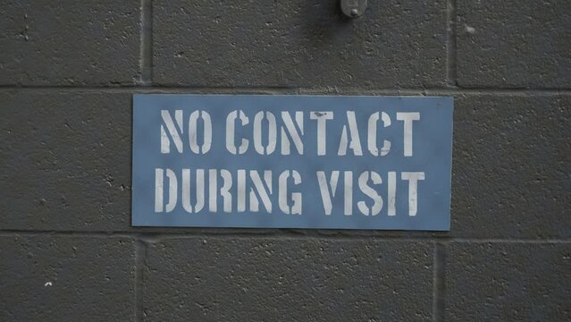 Looping Rack Focus Shot From A Chain Link Fence To A No Contact During Visit Sign In A Prison